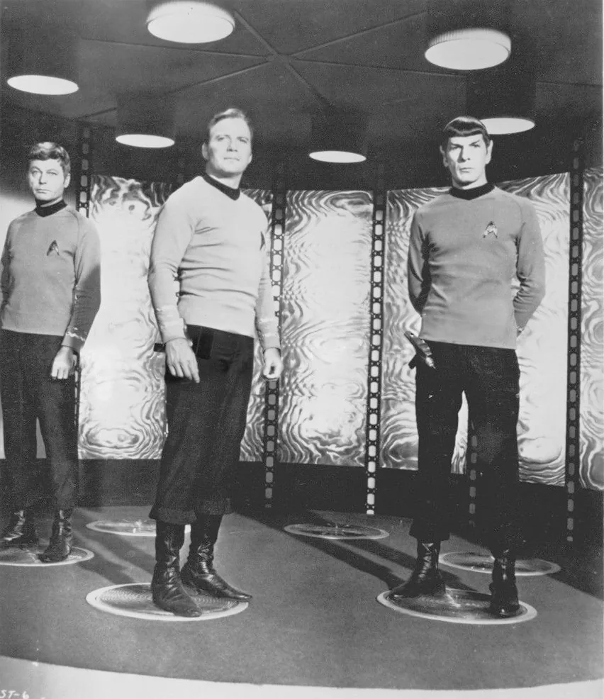 Doktor McCoy, Kaptan Kirk ve Mr. Spock, orijinal Star Trek dizisinde Yıldız Filosu üniformalarıyla ışınlanma odasında; Birincil Direktif kuralına bağlı Starfleet subaylarını temsil ediyor.