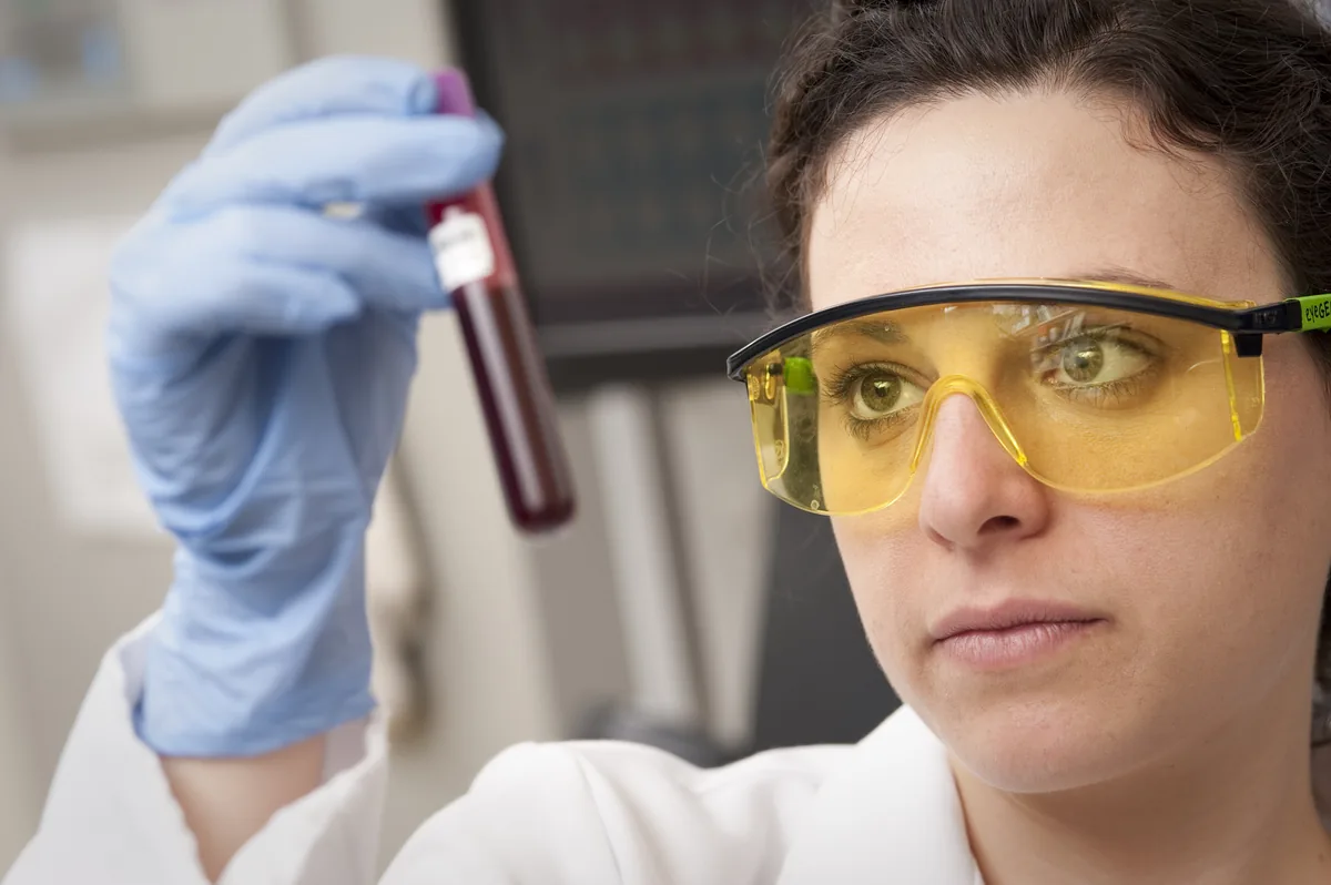 Laboratuvar teknisyeninin koruyucu gözlükle bir kan tüpünü inceleyerek B12 kan testi yaptığı an