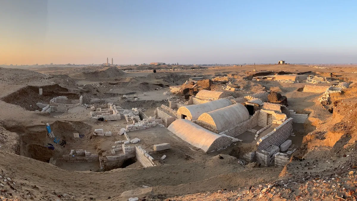 Mısır'ın Oxyrhynchus (Al Bahnasa) antik kentindeki nekropol kazı alanının gün batımında çekilmiş genel görünümü; taş mezar yapıları ve kazı çukurları.