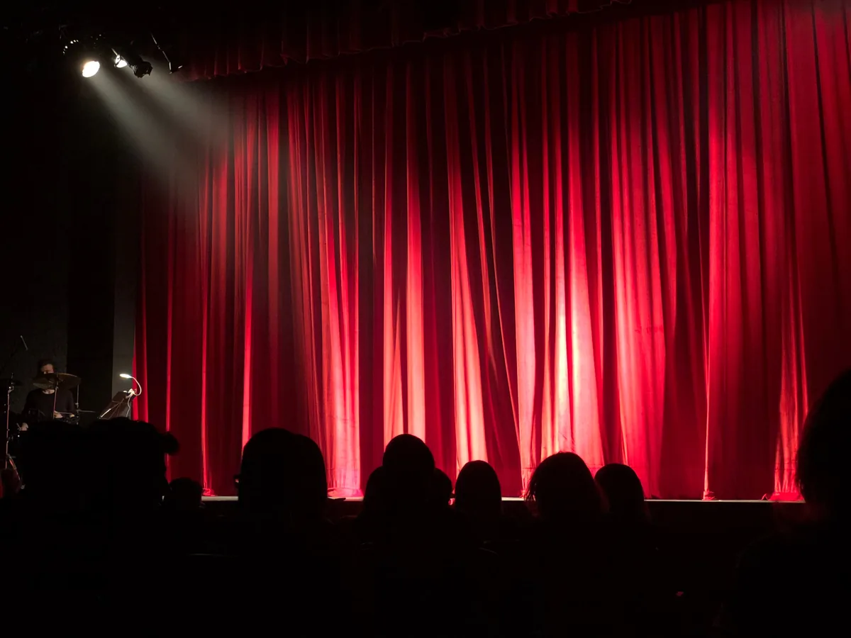 Kırmızı perdenin açılmasını bekleyen tiyatro veya konser salonu izleyicileri