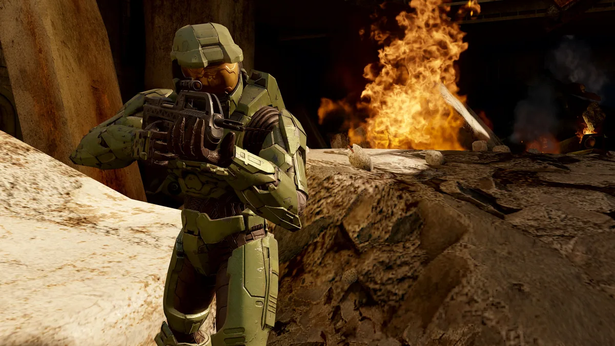 Halo 2 oyununda alevlerin önünde silahını doğrultan yeşil zırhlı Master Chief