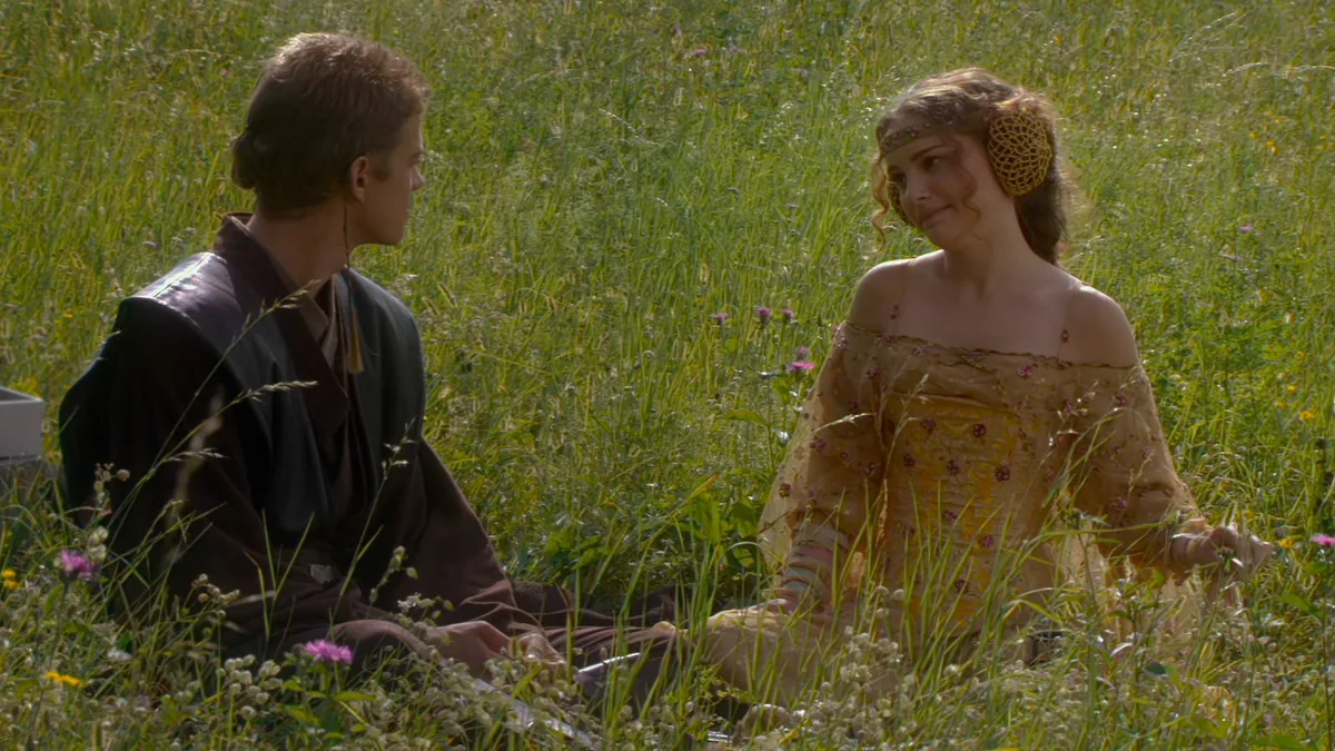 Anakin Skywalker ve Padmé Amidala Naboo çayırında yeşil kırlık üzerinde otururken gülümsüyor, Klonların Saldırısı filminden sahne