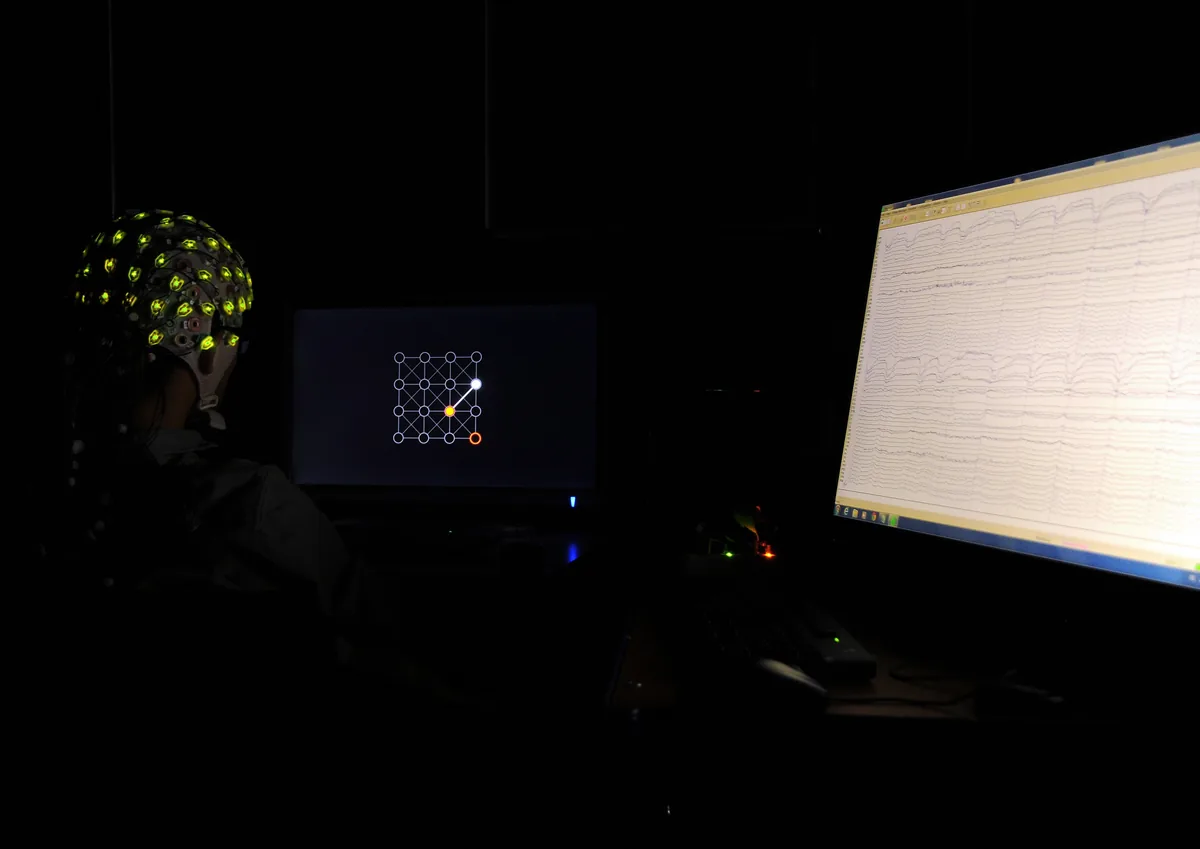 EEG başlığı takan bir katılımcının beyin sinyalleriyle bilgisayarı kontrol ettiği beyin-bilgisayar arayüzü deneyi, yanında canlı EEG dalga formu ekranı