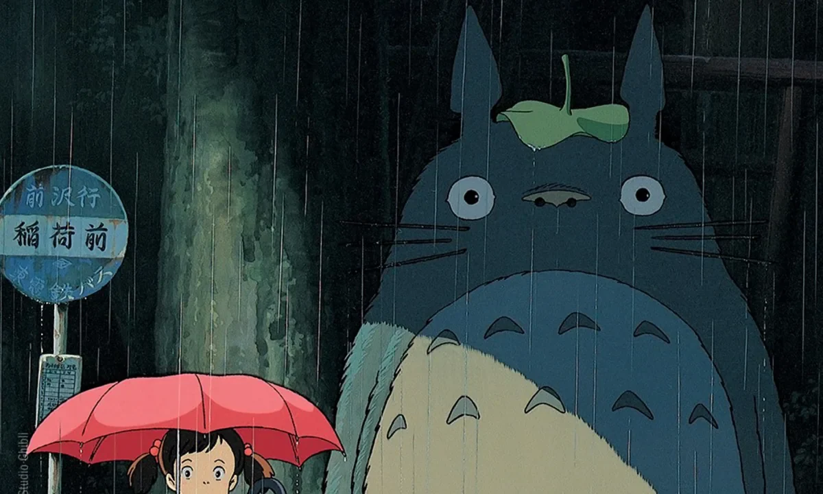Komşum Totoro filminin resmi afişi: yağmurlu otobüs durağında şemsiyeli Satsuki ve dev orman ruhu Totoro