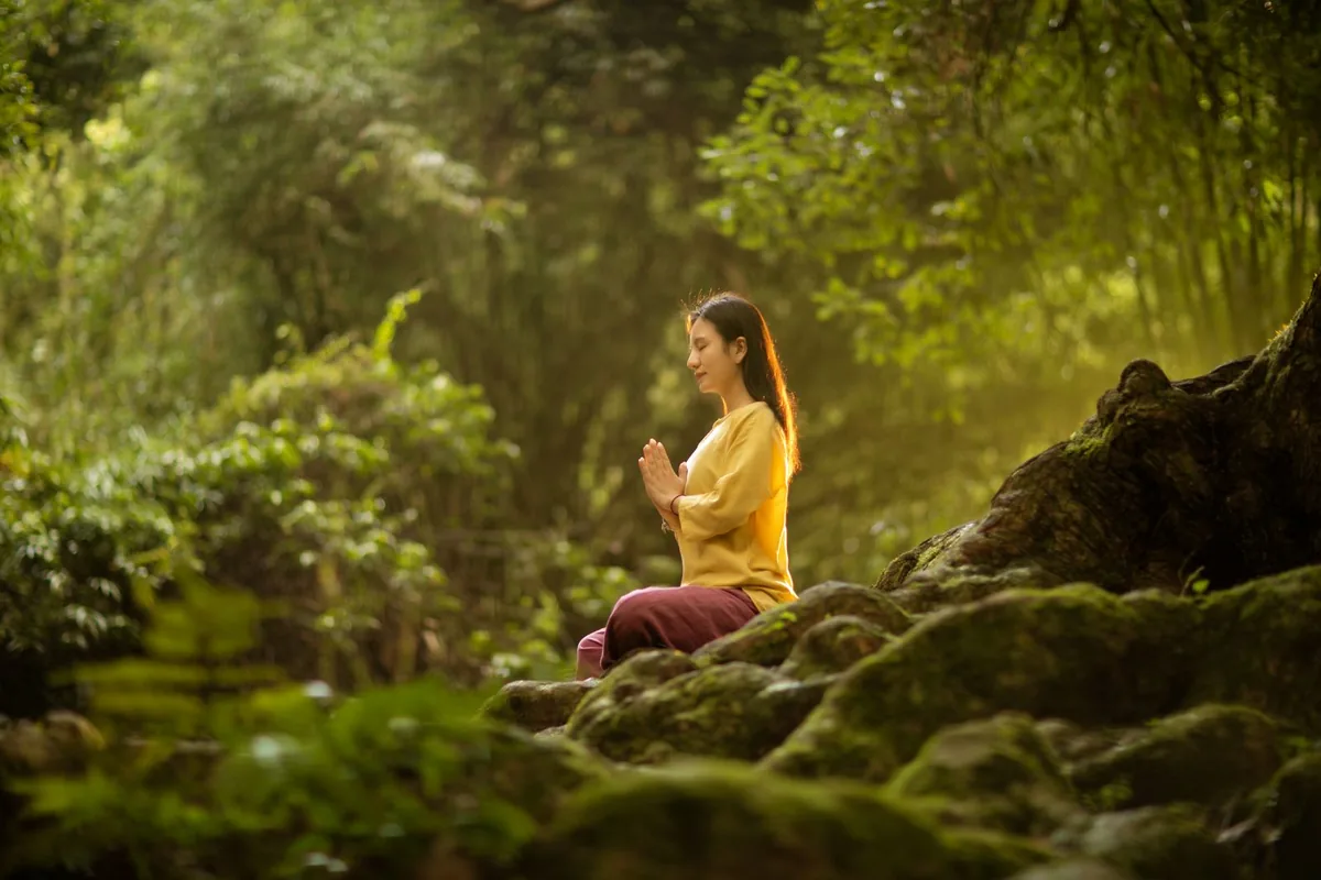Doğada, yeşil bir ormanda huzurlu şekilde meditasyon ve nefes egzersizi yapan bir kadın
