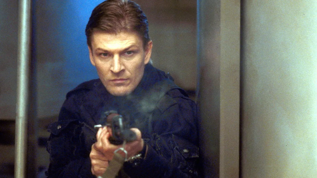 Sean Bean, GoldenEye filminde Alec Trevelyan/006 karakteri olarak silah doğrultmuş halde, resmi film karesi