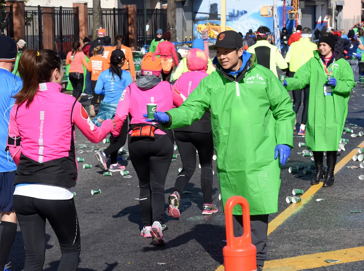 Maraton parkurunda koşarken yeşil sporcu içeceği bardağını alan koşucular grubu