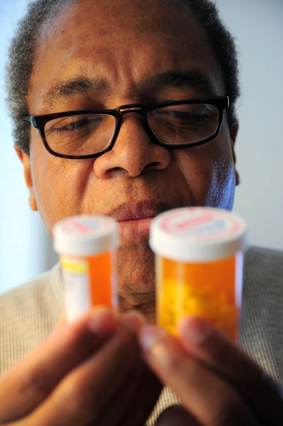 İlaç kutusunu inceleyen orta yaşlı bir hasta, statin yan etkileri konusunda tereddütlü bir ifadeyle reçeteli ilaç şişelerine bakıyor
