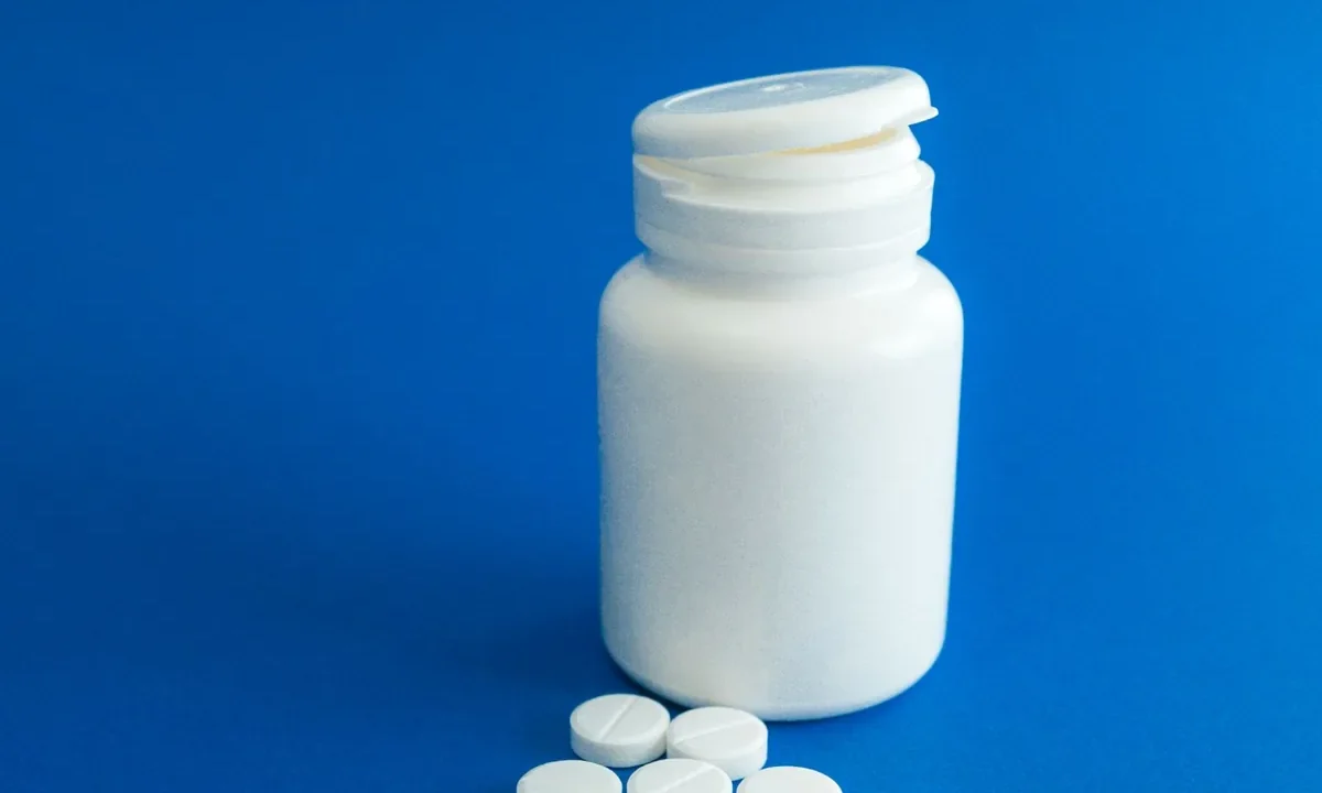 Beyaz statin (kolesterol düşürücü ilaç) tabletleri ve yanında duran ilaç şişesi, statin yan etkileri ne zaman endişelenmeli sorusunu temsil ediyor