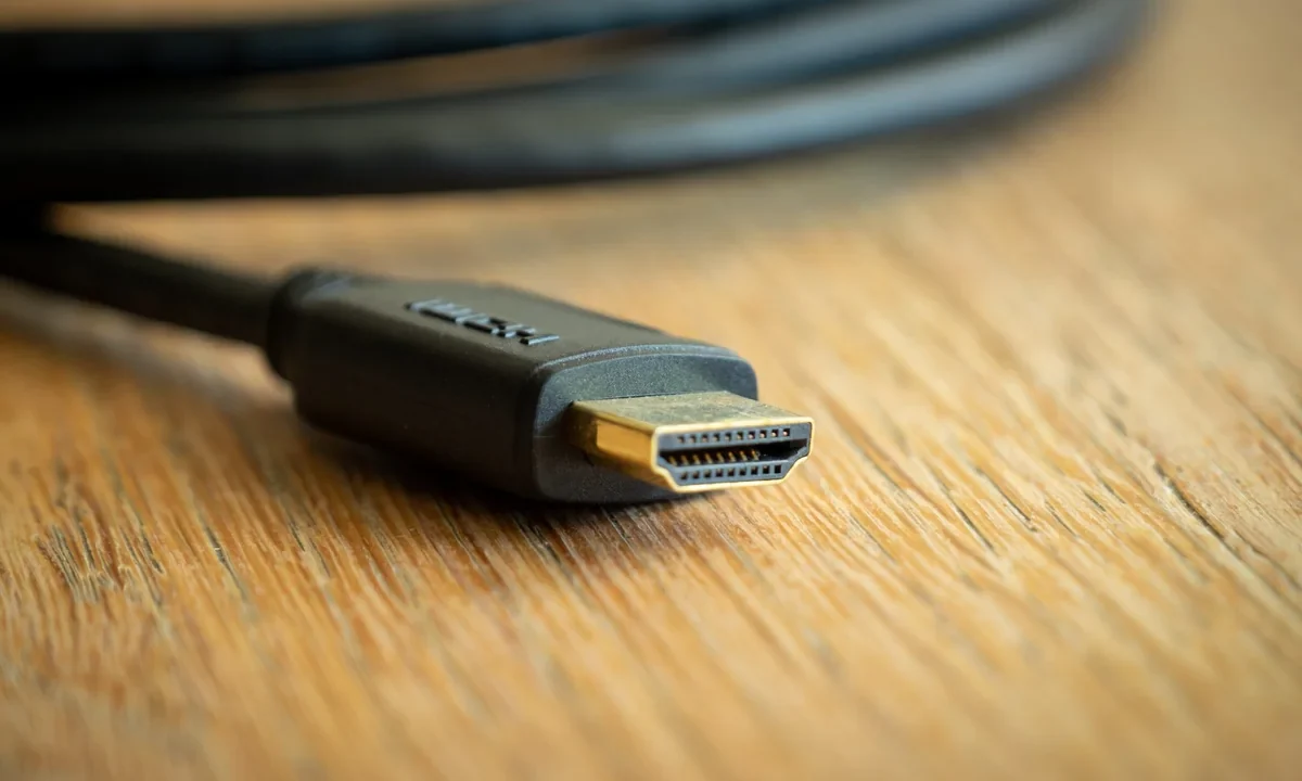 Ahşap zemin üzerinde altın kaplamalı uçlu bir HDMI kablosunun konektörü yakın planda; pahalı HDMI kablo görüntü kalitesini artırır mı sorusunu görsel olarak temsil eder
